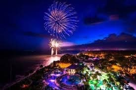 Coastal fireworks display over illuminated shoreline at night