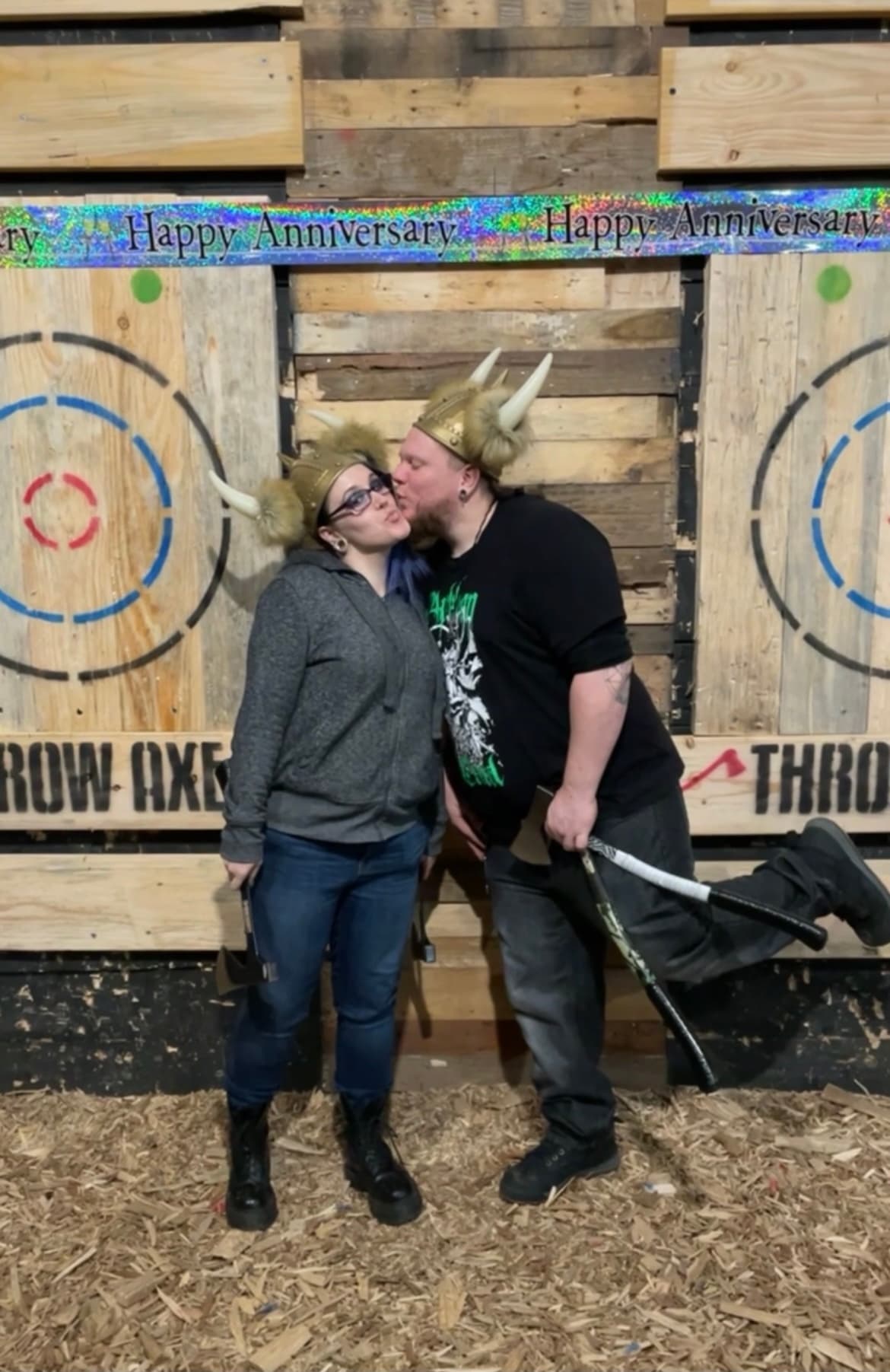 Couple kissing at indoor axe throwing lane wearing helmet