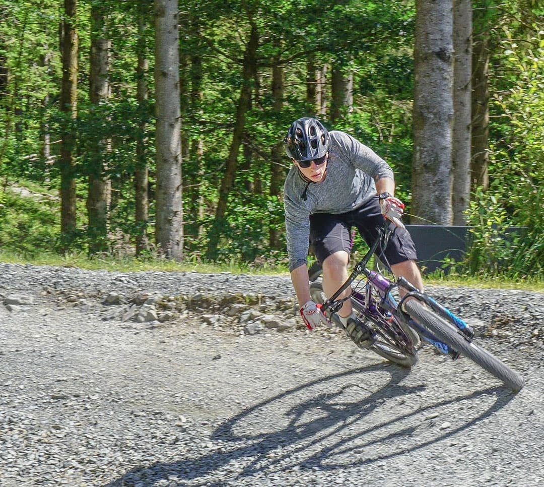 Mountain biker carving gravel trail through sunlit pine forest
