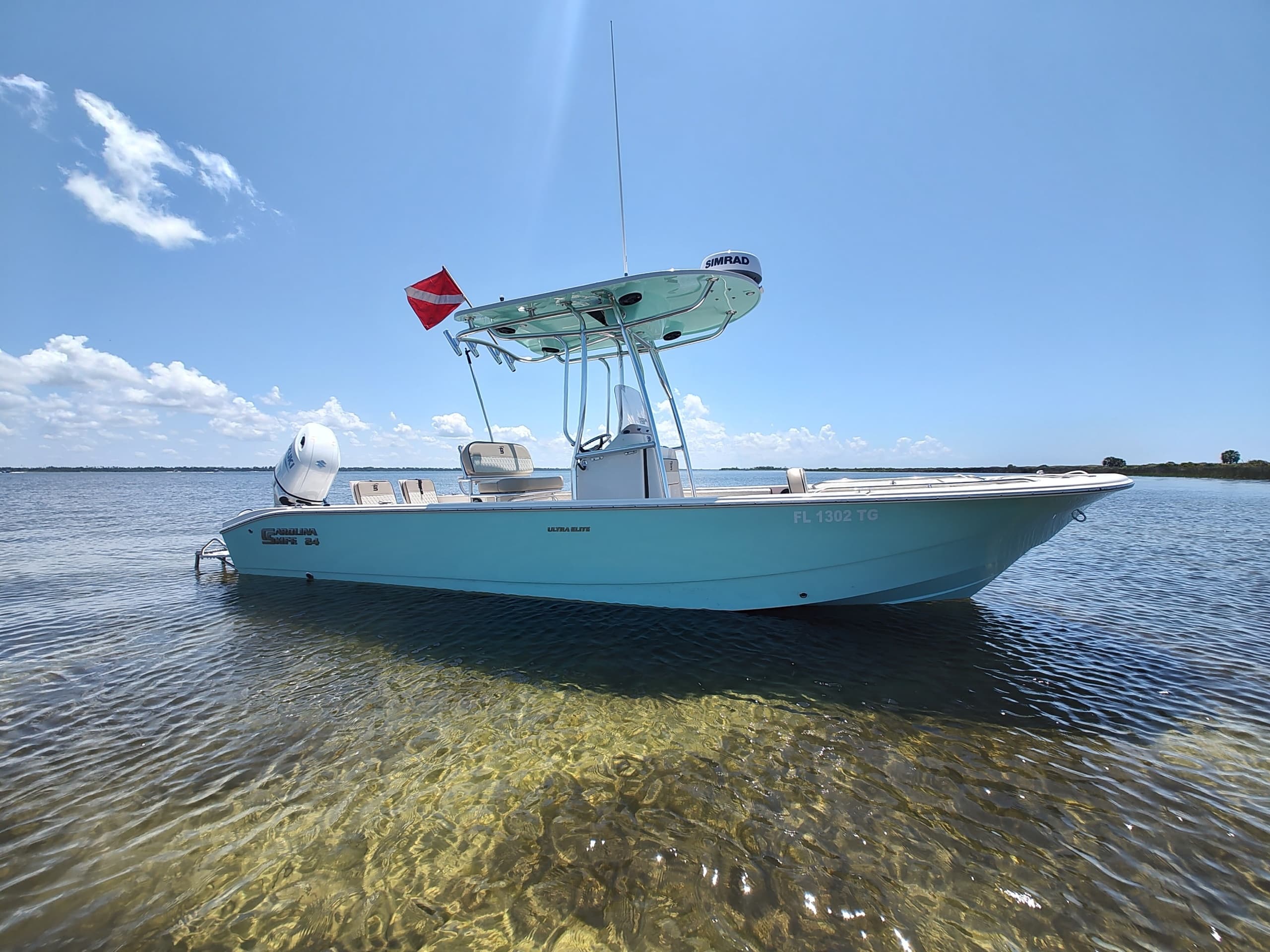 Center console boat beached in shallow clear flats with diving flag