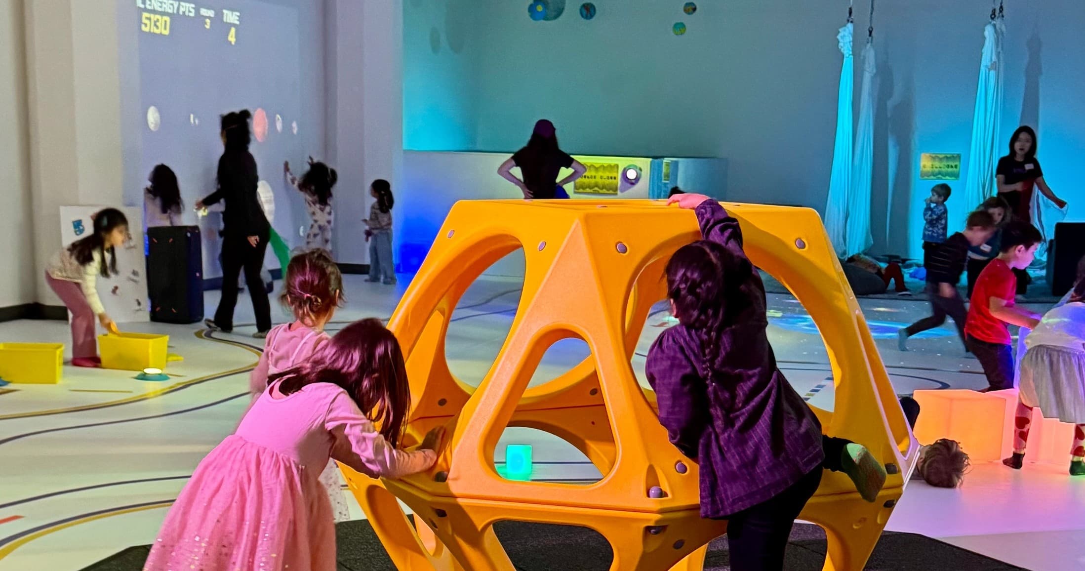 Children climbing a yellow geometric play structure in indoor exhibit
