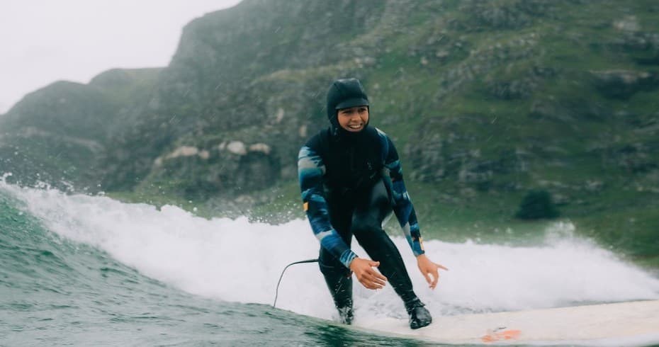 Surfer in wetsuit riding a wave near rugged coastal hillside