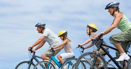 Family cycling together on coastal trail, helmets and smiles