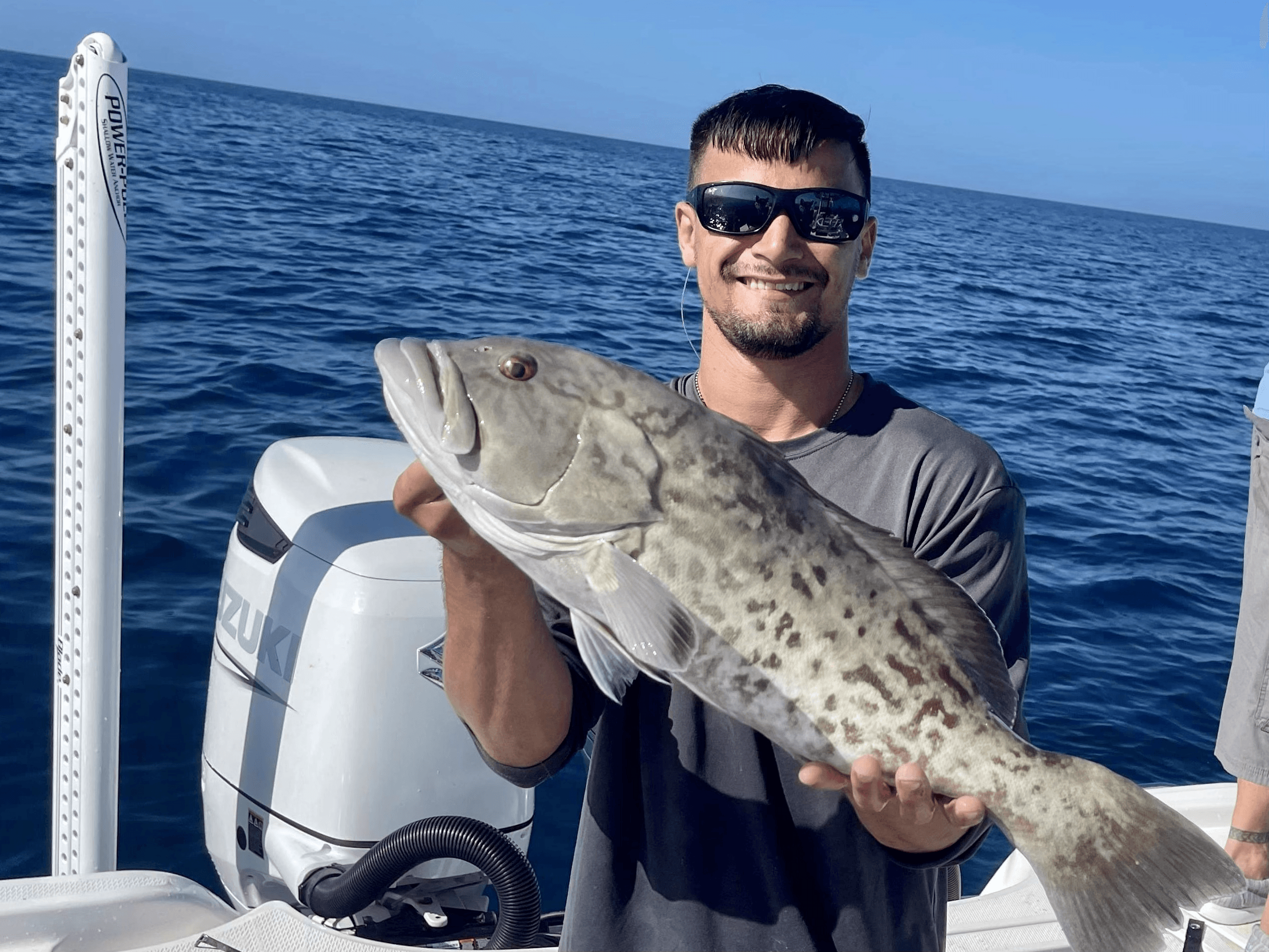 Angler holding large grouper on charter boat offshore in clear sea