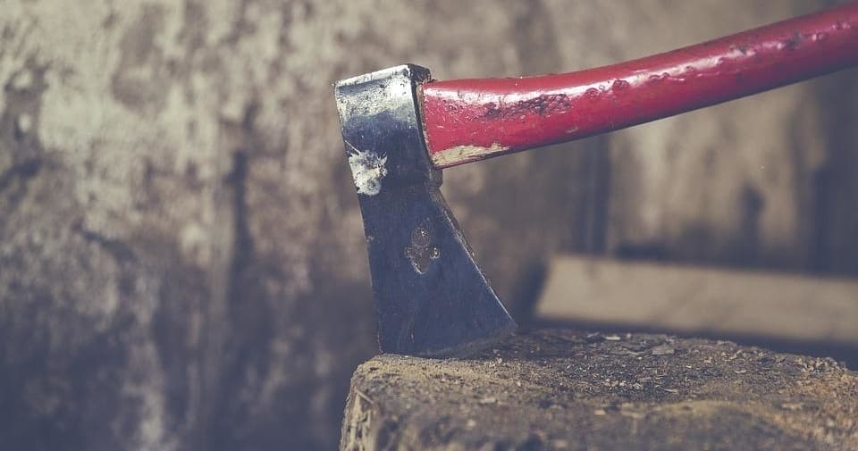 Red-handled axe embedded in chopping block at rustic cabin