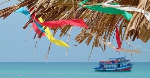 Tropical beach boat seen under thatch with colorful flags, seaside