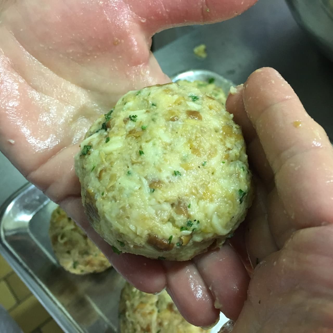 Chef shaping herb meatball by hand in kitchen prep tray