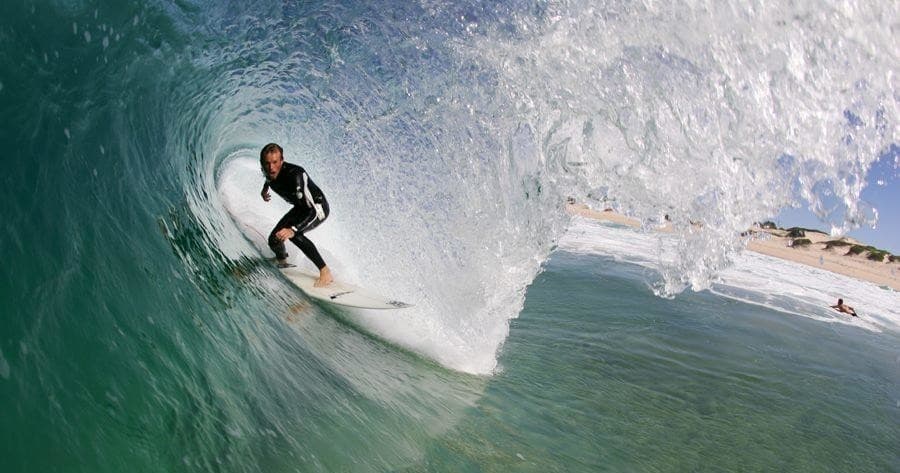 Surfer in a barreling wave tube on clear green ocean shore