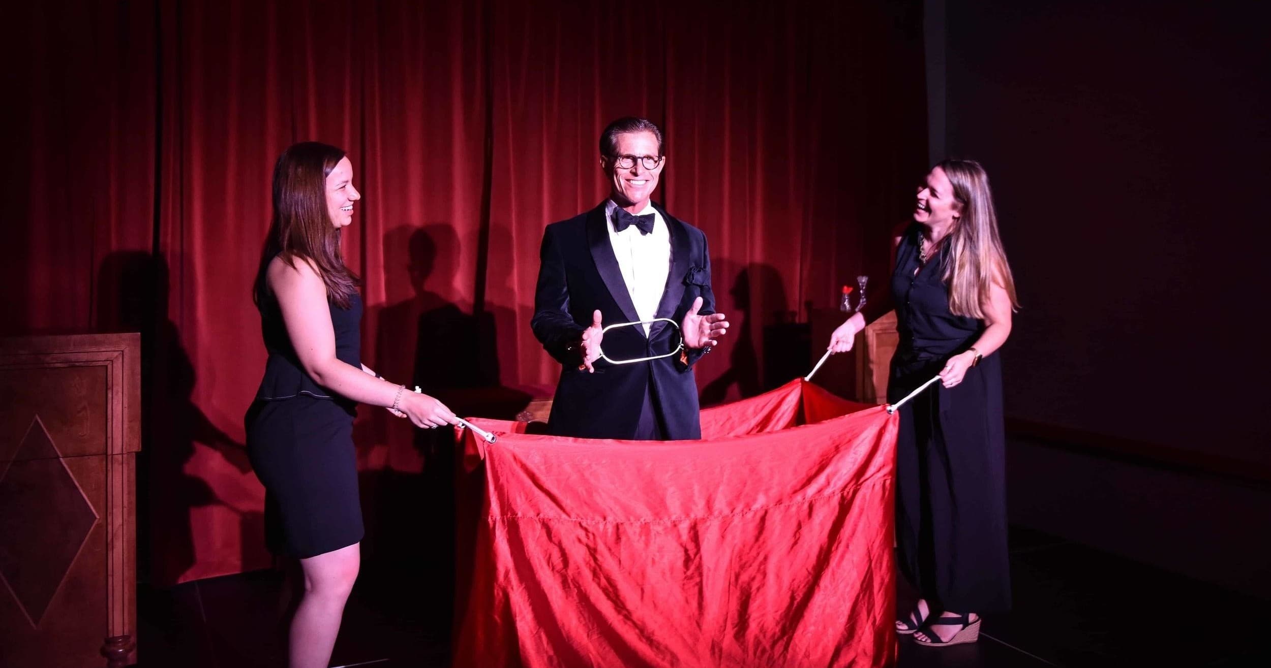 Magician performing illusion with assistants onstage under red drape in Atlanta