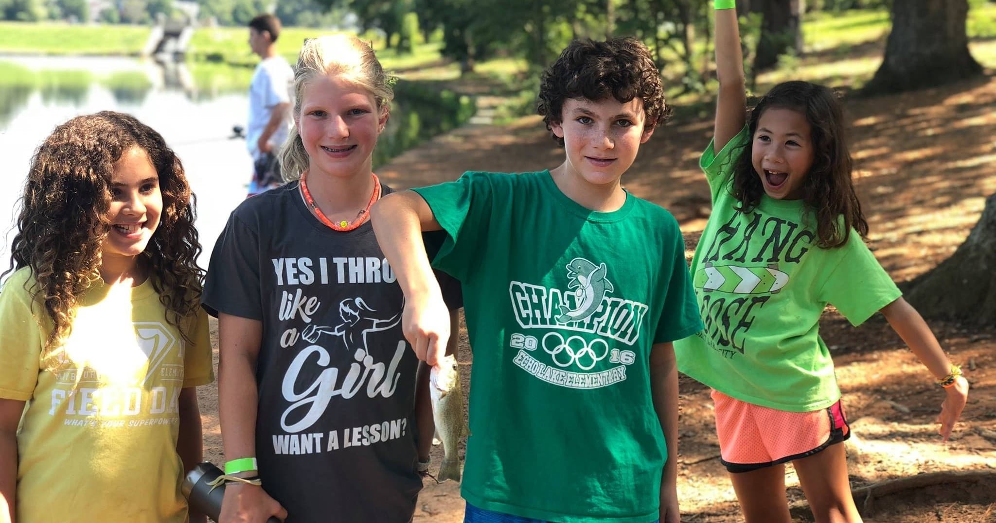 Kids posing lakeside at summer camp on grassy park trail