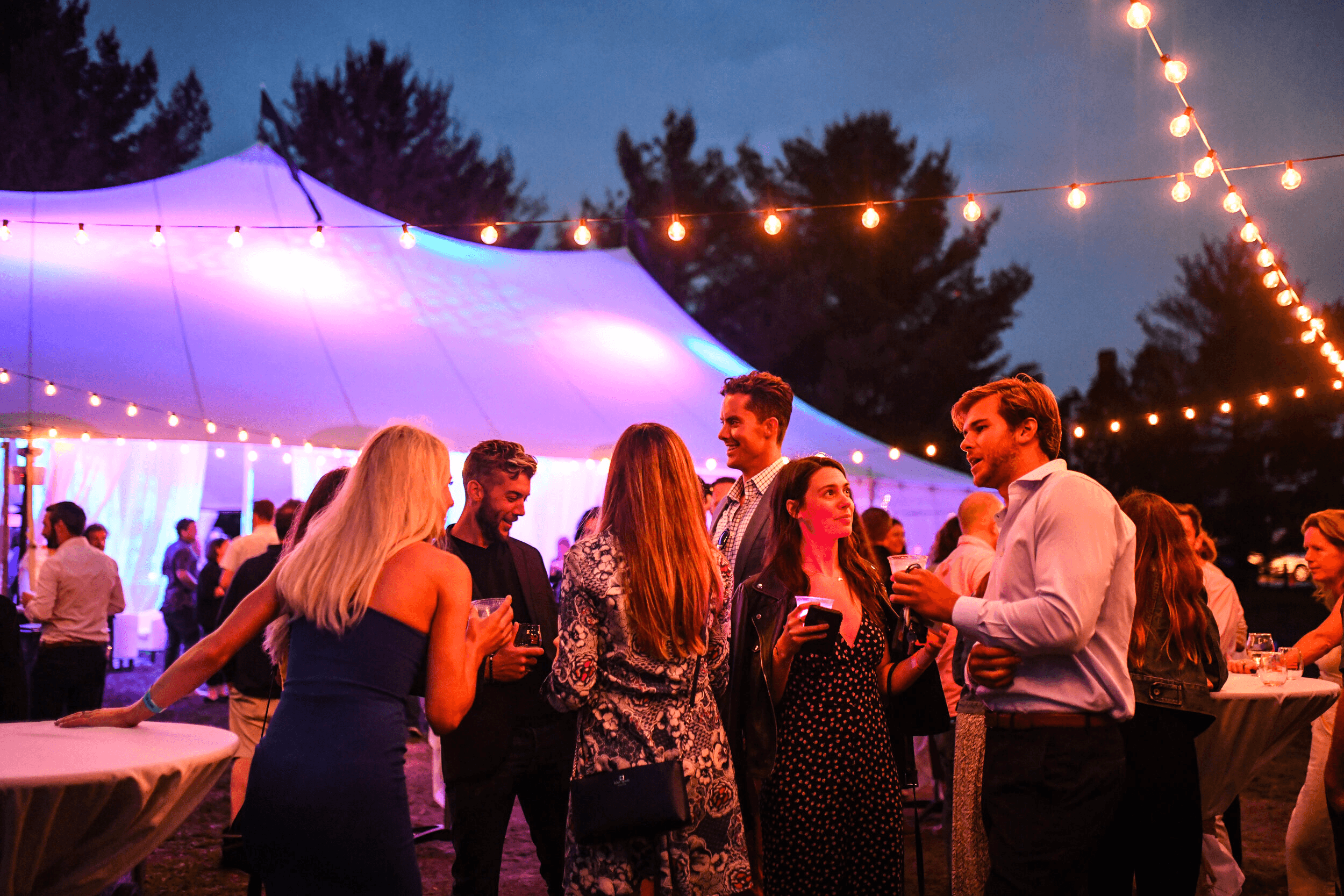 Evening outdoor tent party with string lights and mingling guests