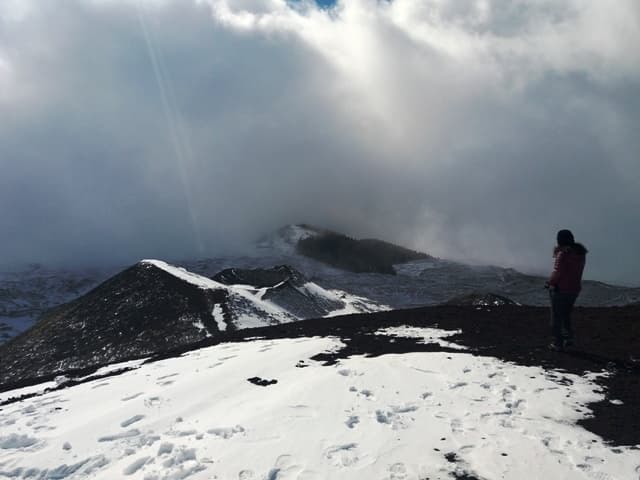 Hiker on snowy volcanic ridge with sweeping clouds, Etna ascent
