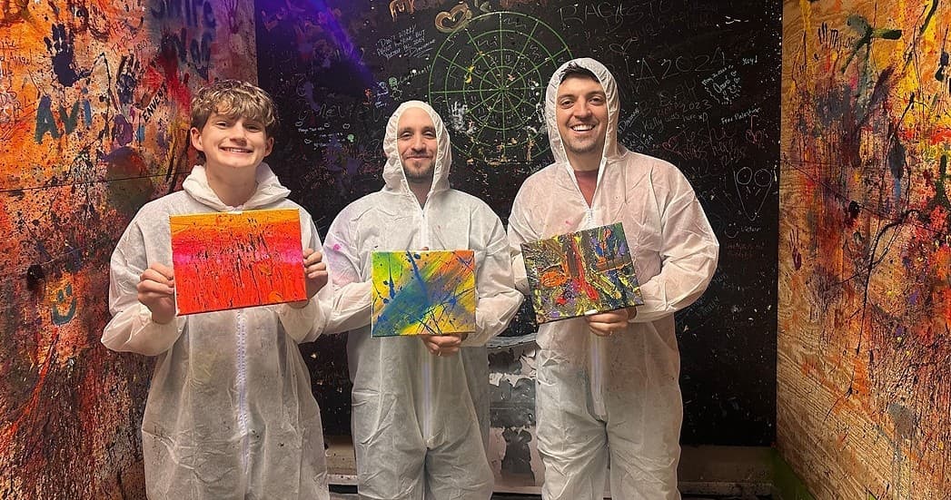 Three participants holding splatter paintings in indoor art smash room