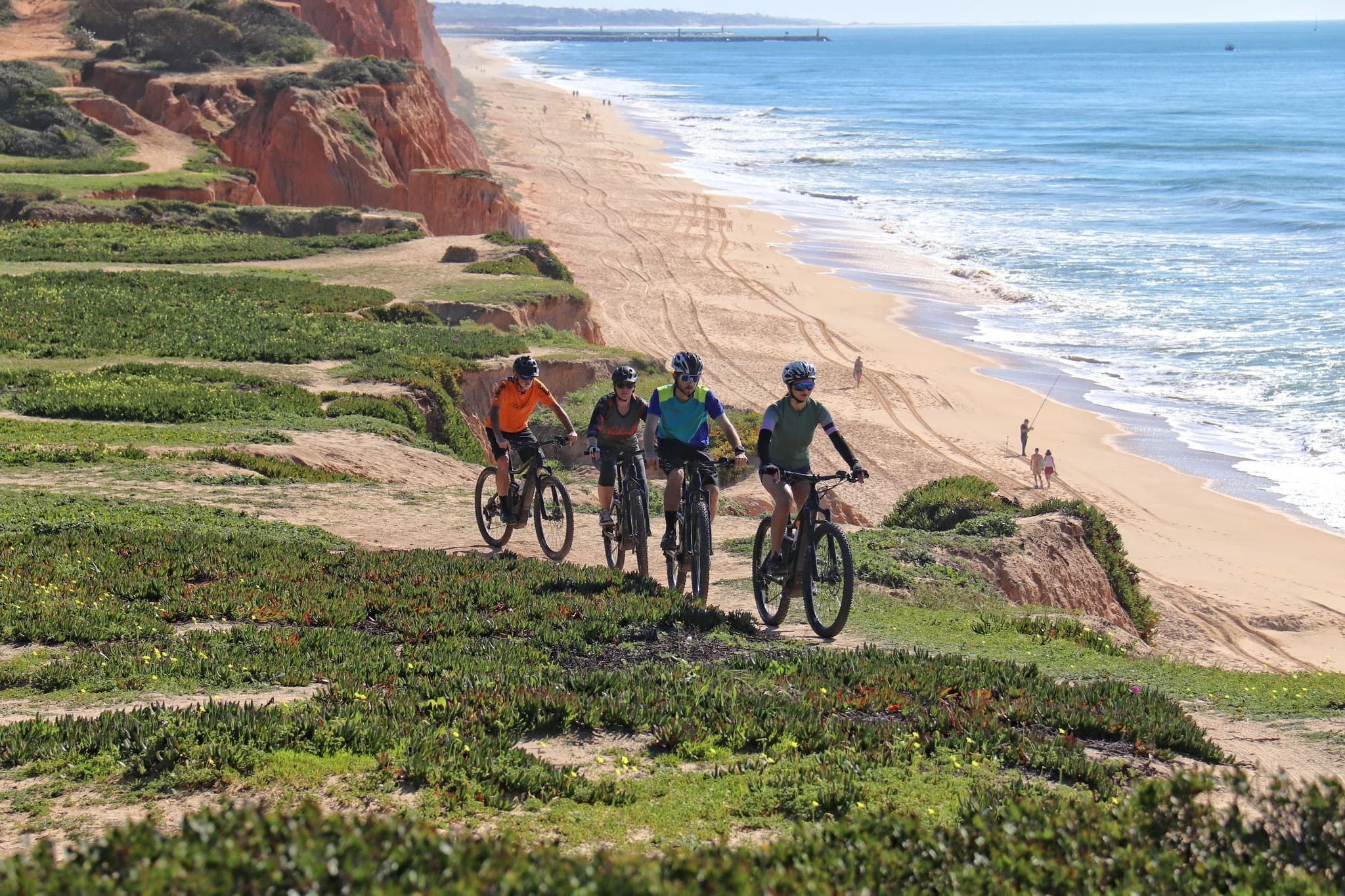 Cyclists riding coastal cliffs with ocean views on sunny trail