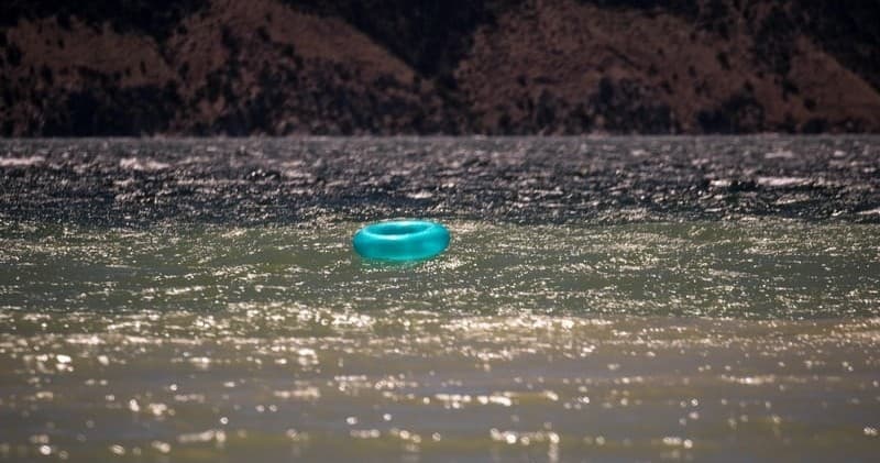 Blue inner tube floating on sunlit lake near shore