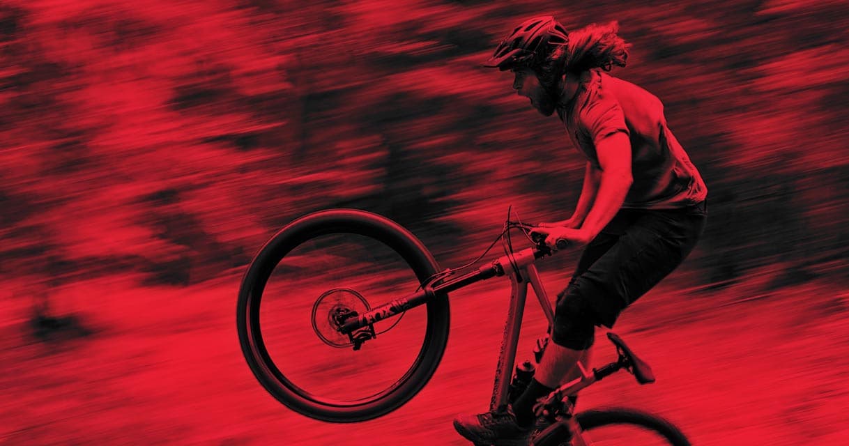 Mountain biker launching a jump on a wooded downhill trail