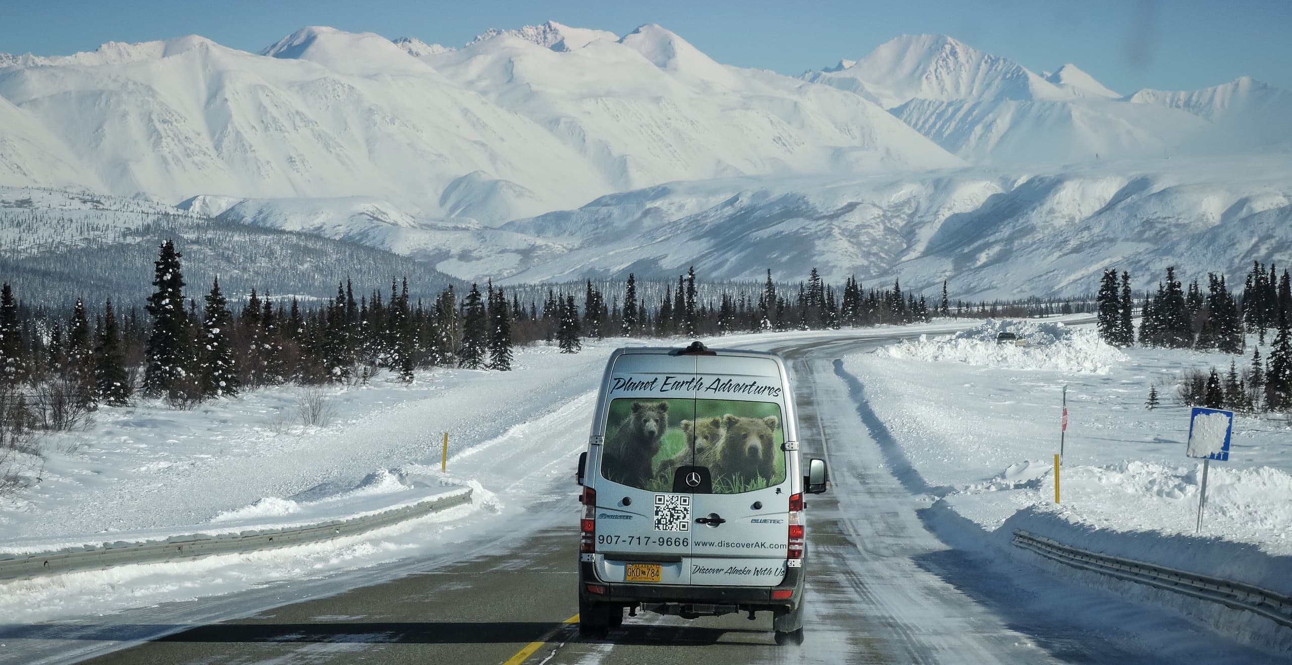 Tour van driving on snowy Alaskan highway toward mountain peaks