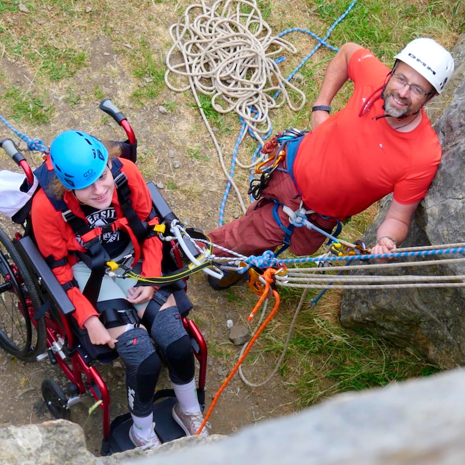 Adaptive climber in harness being belayed on rocky outdoor crag