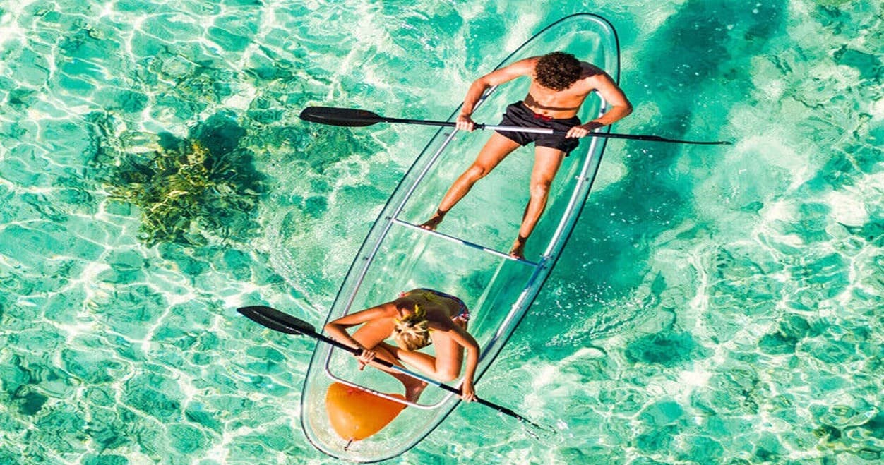 Couple paddling in clear turquoise sea in transparent kayak