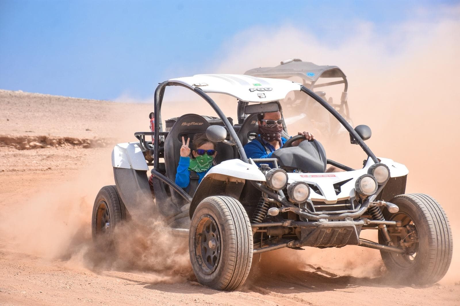 White dune buggy kicking up sand across arid desert landscape in action