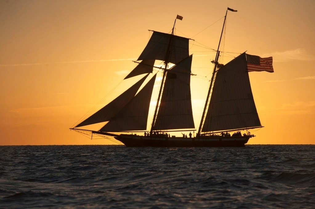 Tall ship silhouetted sailing at sunset on open ocean