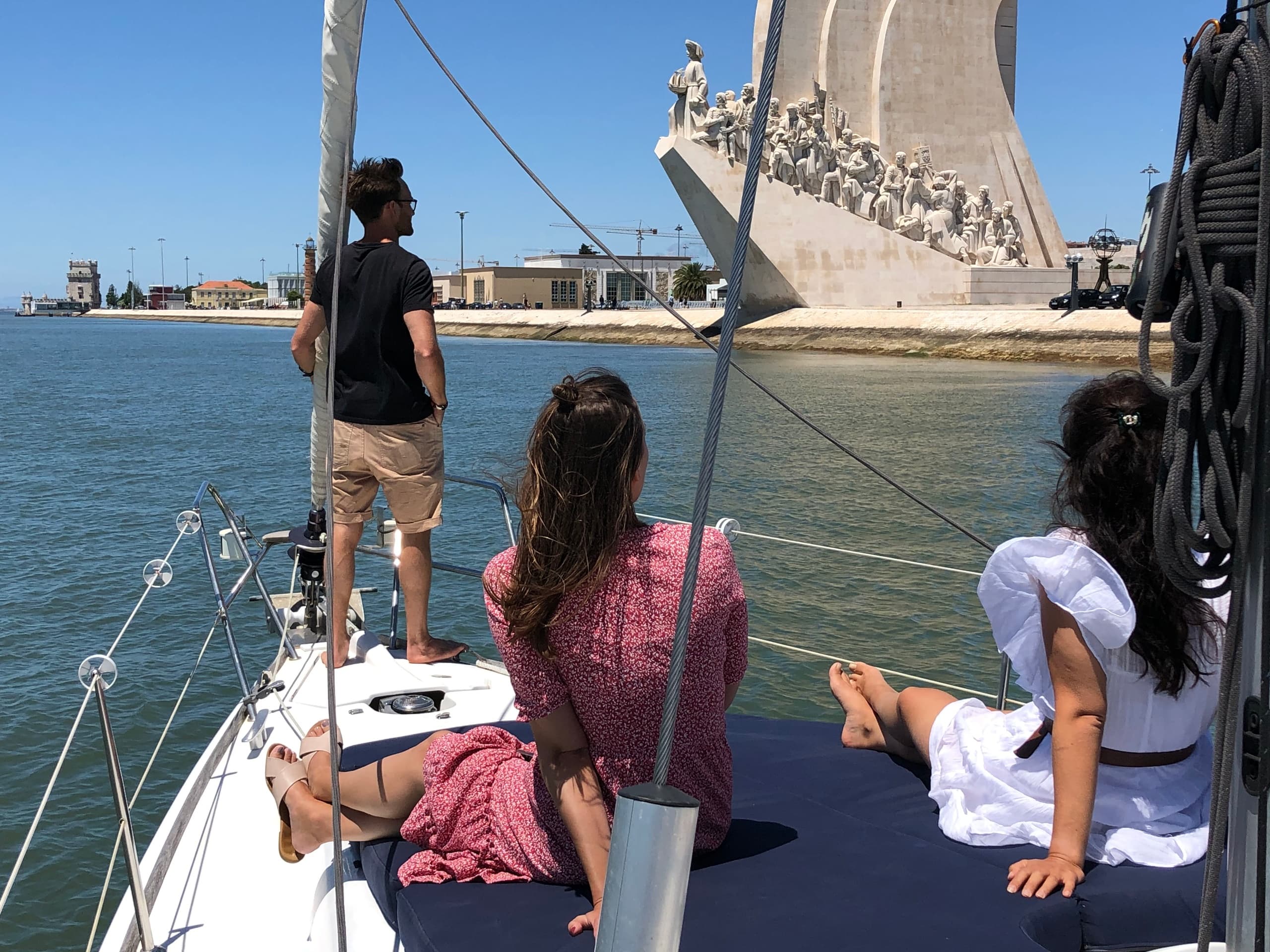 Passengers enjoying daytime sail past Lisbon monument on yacht
