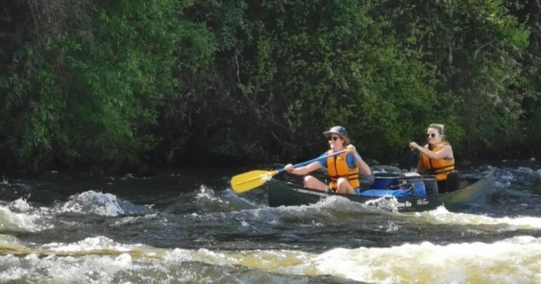Pair of paddlers navigating fast whitewater on forested river
