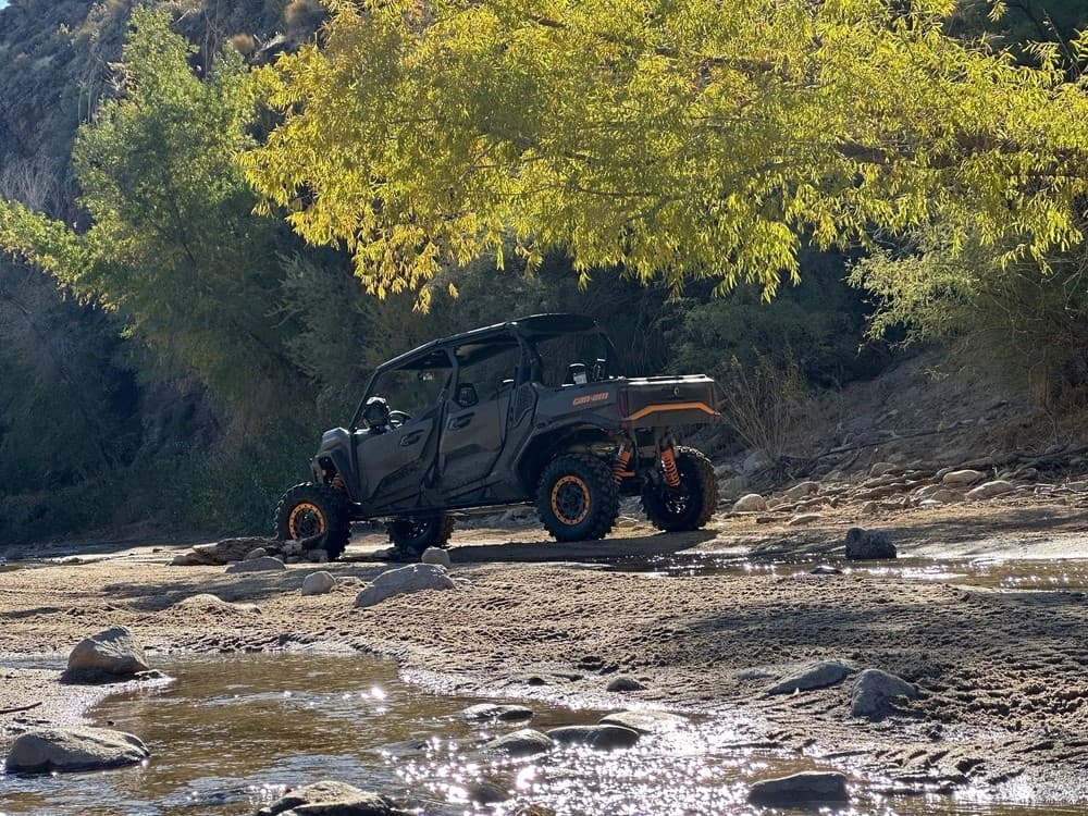 UTV crossing shallow creek amid autumn trees on rugged trail