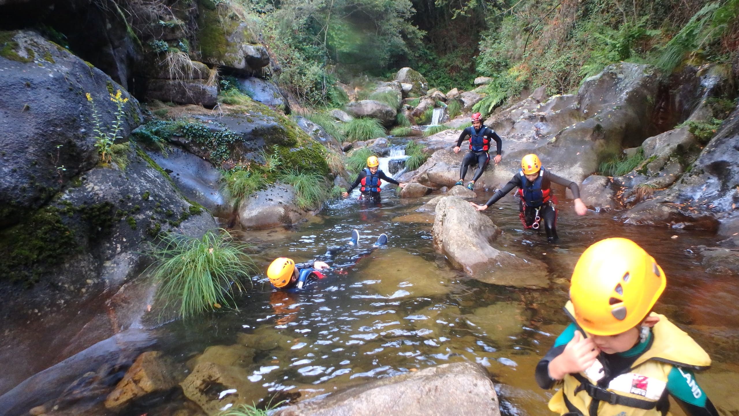 Group canyoning through rocky stream with helmets and ropes