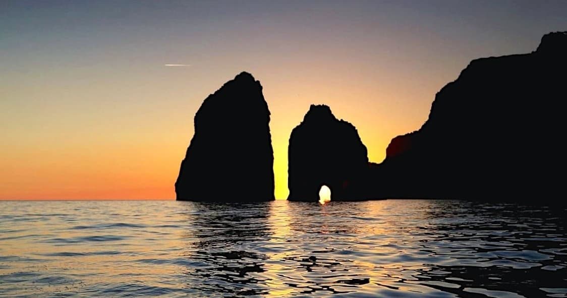 Boat cruising past dramatic sea stacks at sunset on Mediterranean
