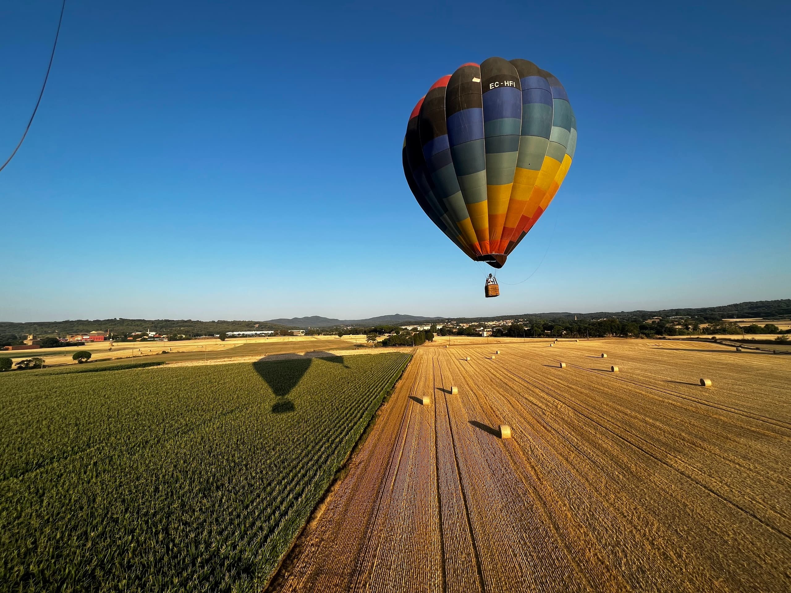 Multicolor hot air balloon flying over harvested fields with long shadows, Emporda