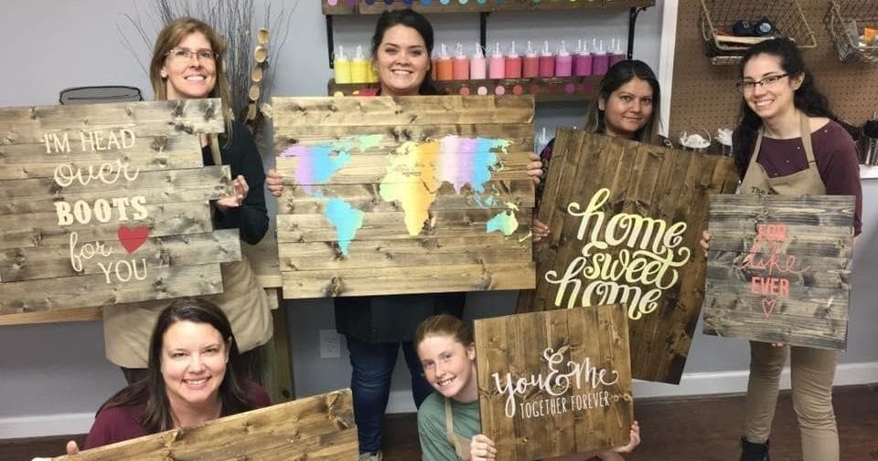 Group holding finished rustic signs in indoor painting workshop