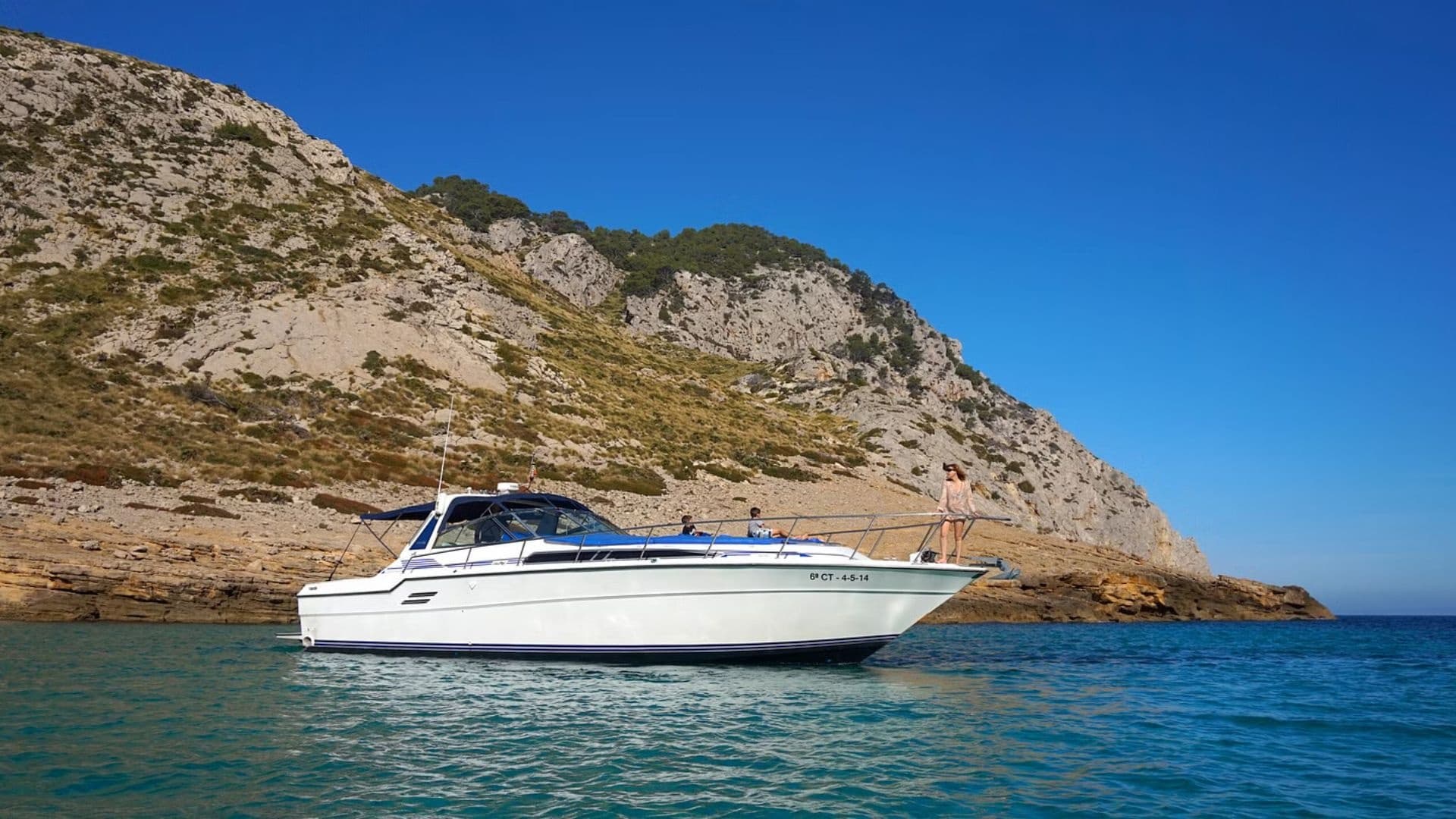Motorboat cruising near rocky Mediterranean coast under blue sky