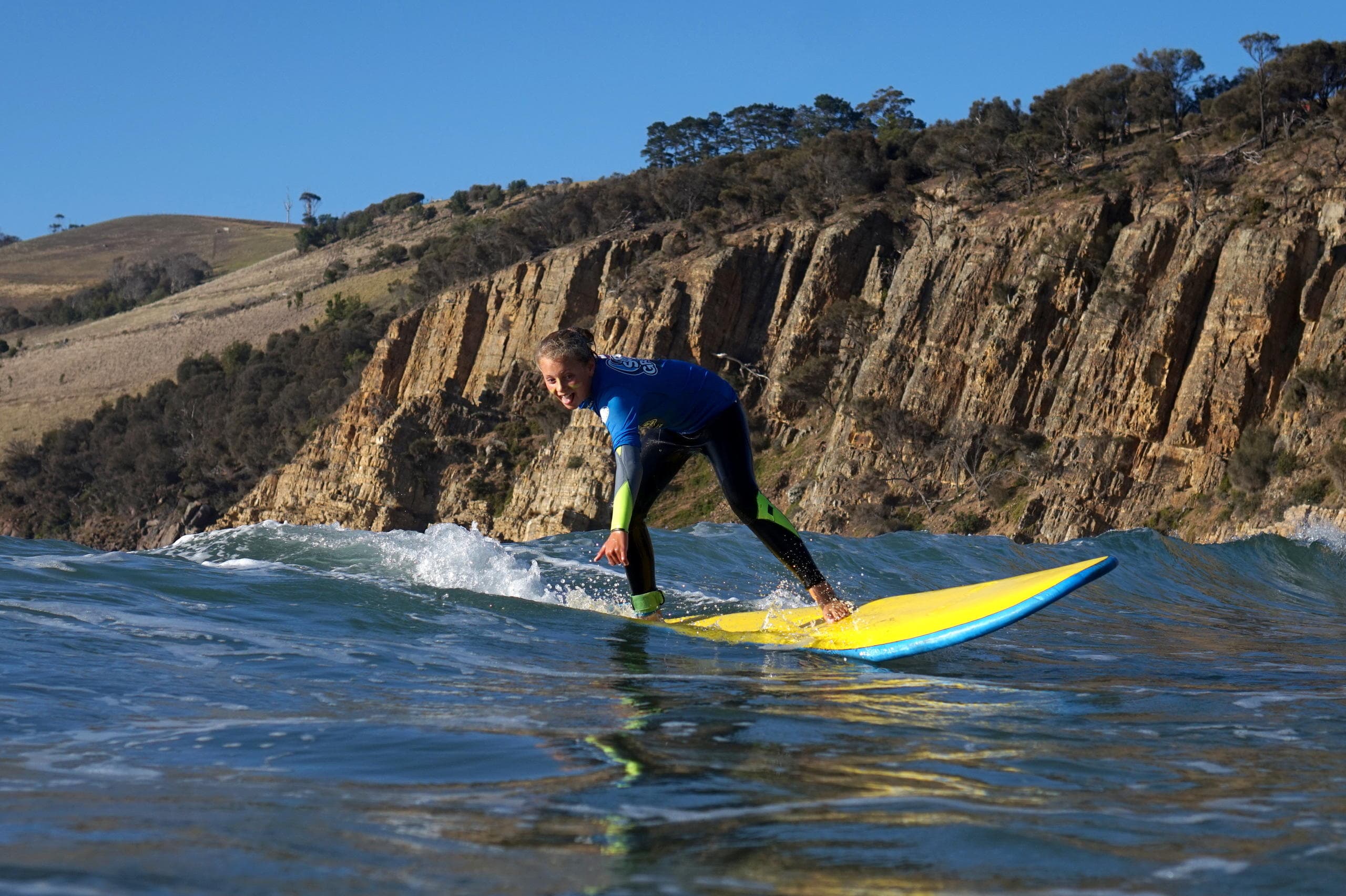 Surfer riding wave near coastal cliffs during sunny session