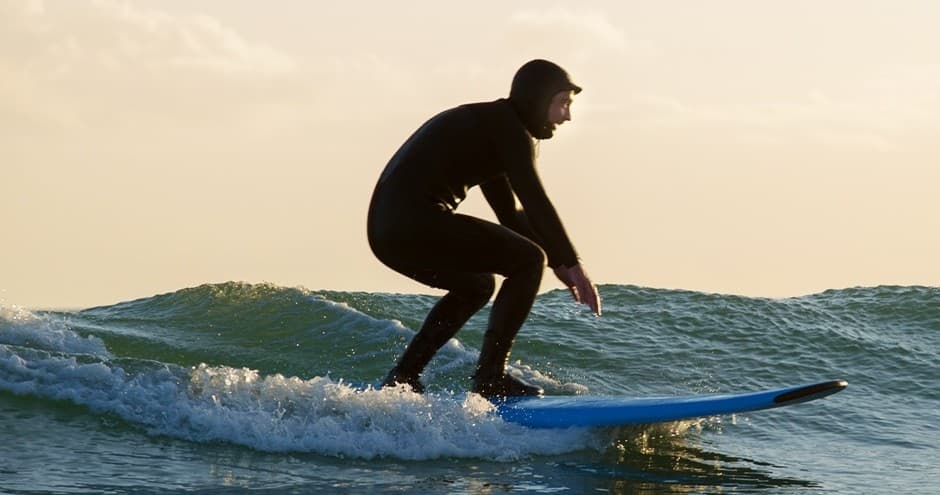 Surfer riding ocean wave at golden sunset on coastal waters