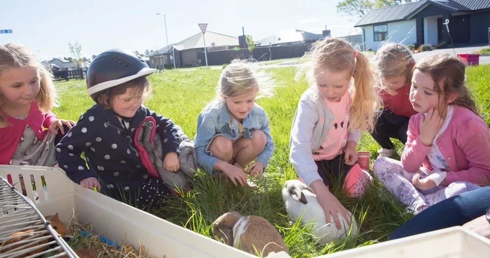 Children petting farmyard animals on grassy suburban field