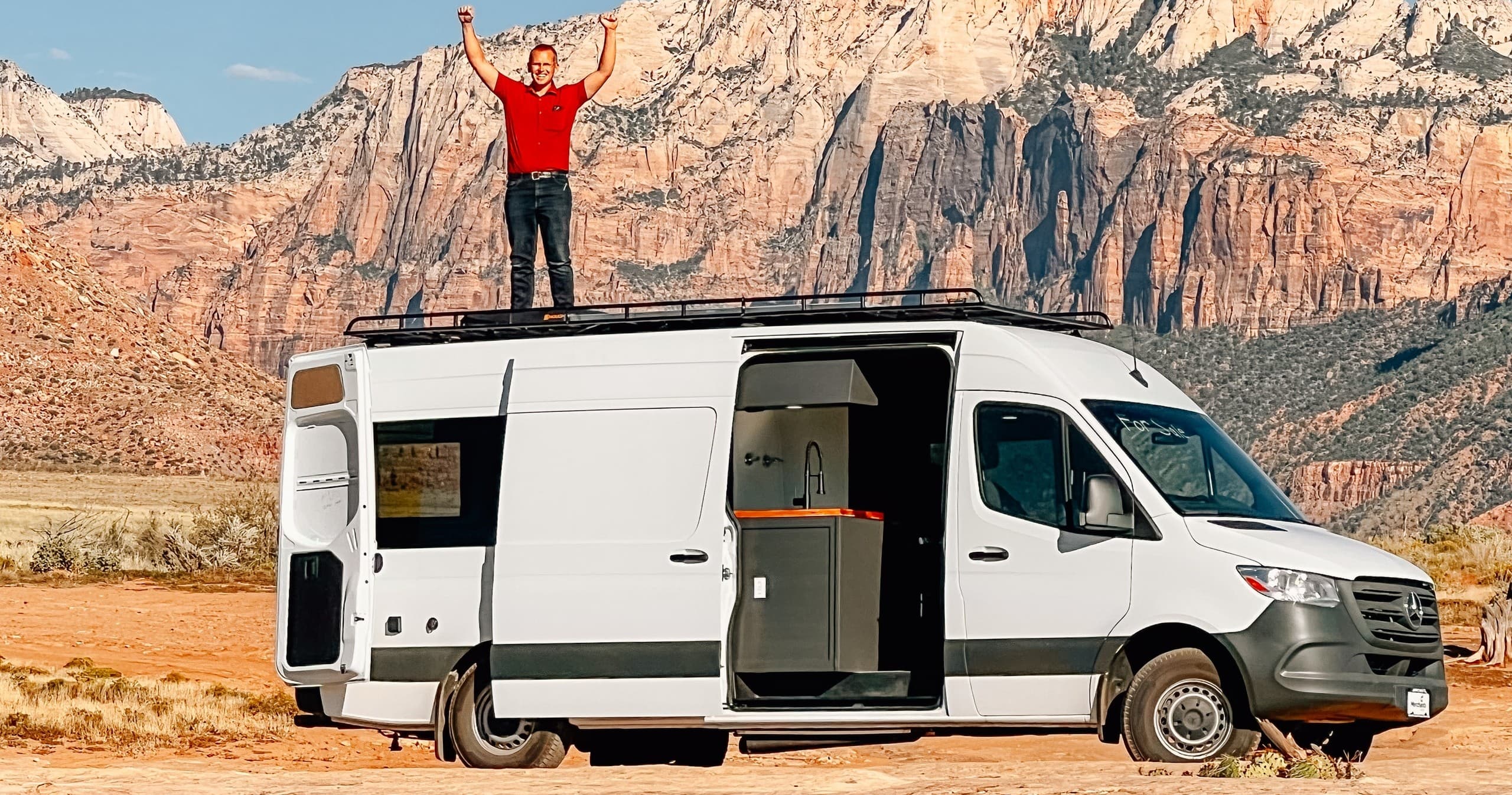 Camper van with person on roof by red cliffs in desert