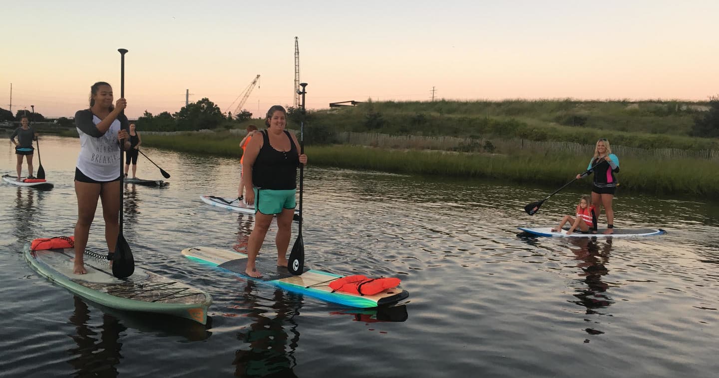 Group stand-up paddleboarding in marshy estuary at dusk