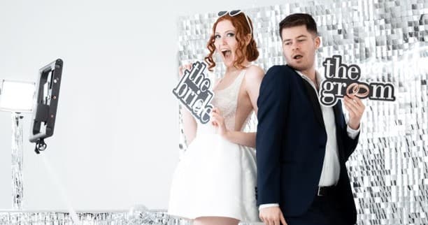 Bridal couple posing in wedding photo booth with sparkled backdrop