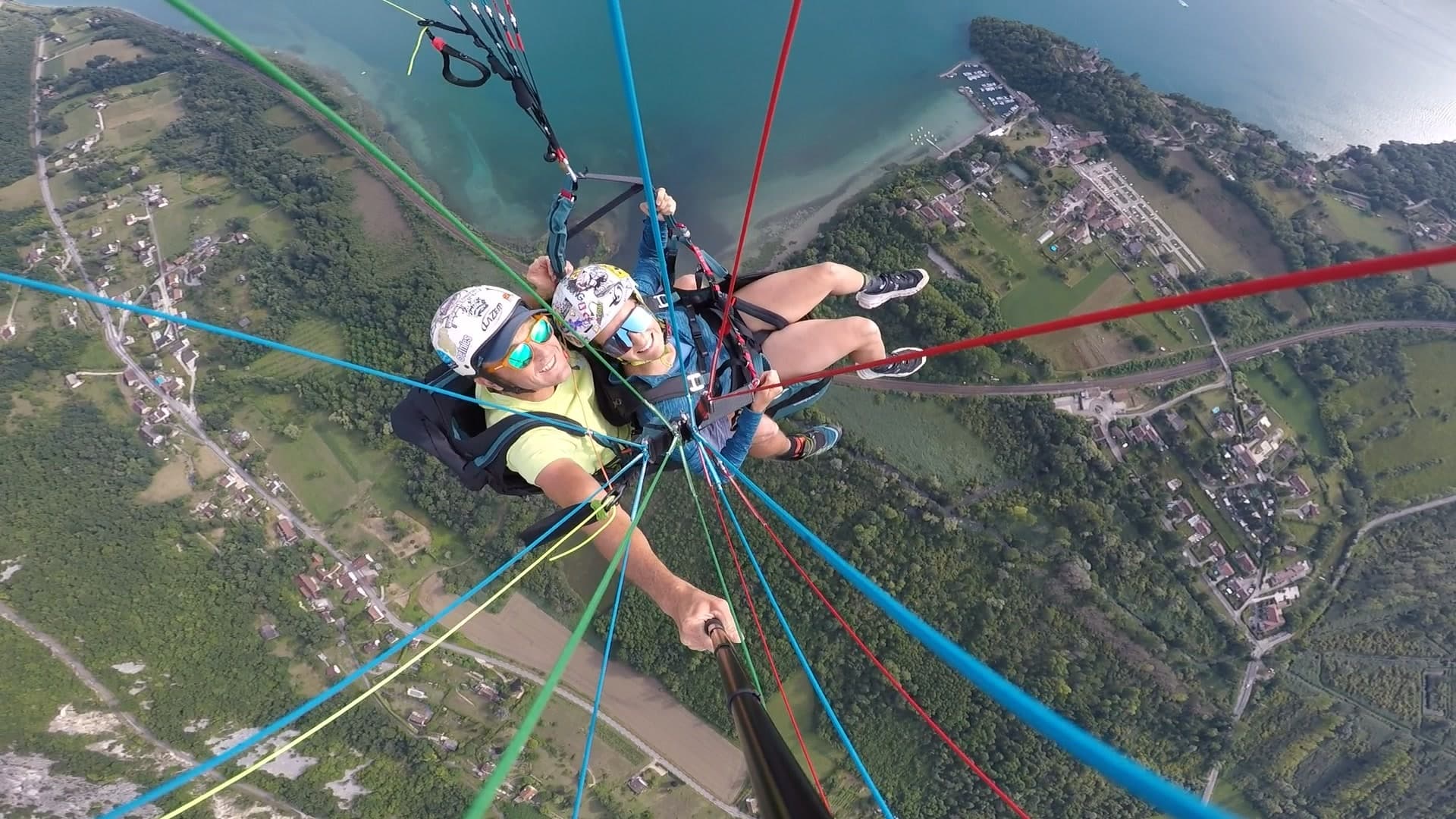Aerial tandem paragliding over lakeside town with colorful lines