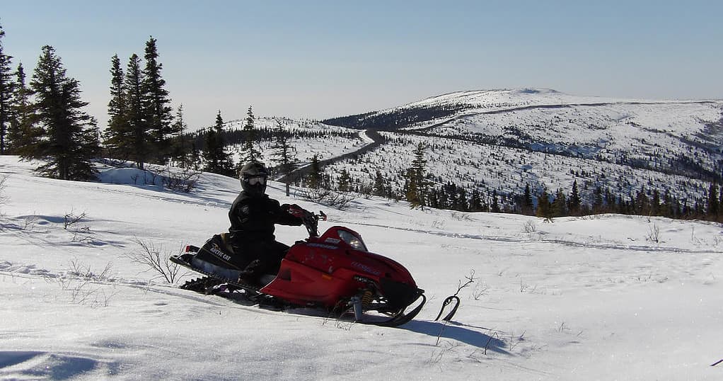 Rider on red snowmobile carving through open snowy tundra landscape