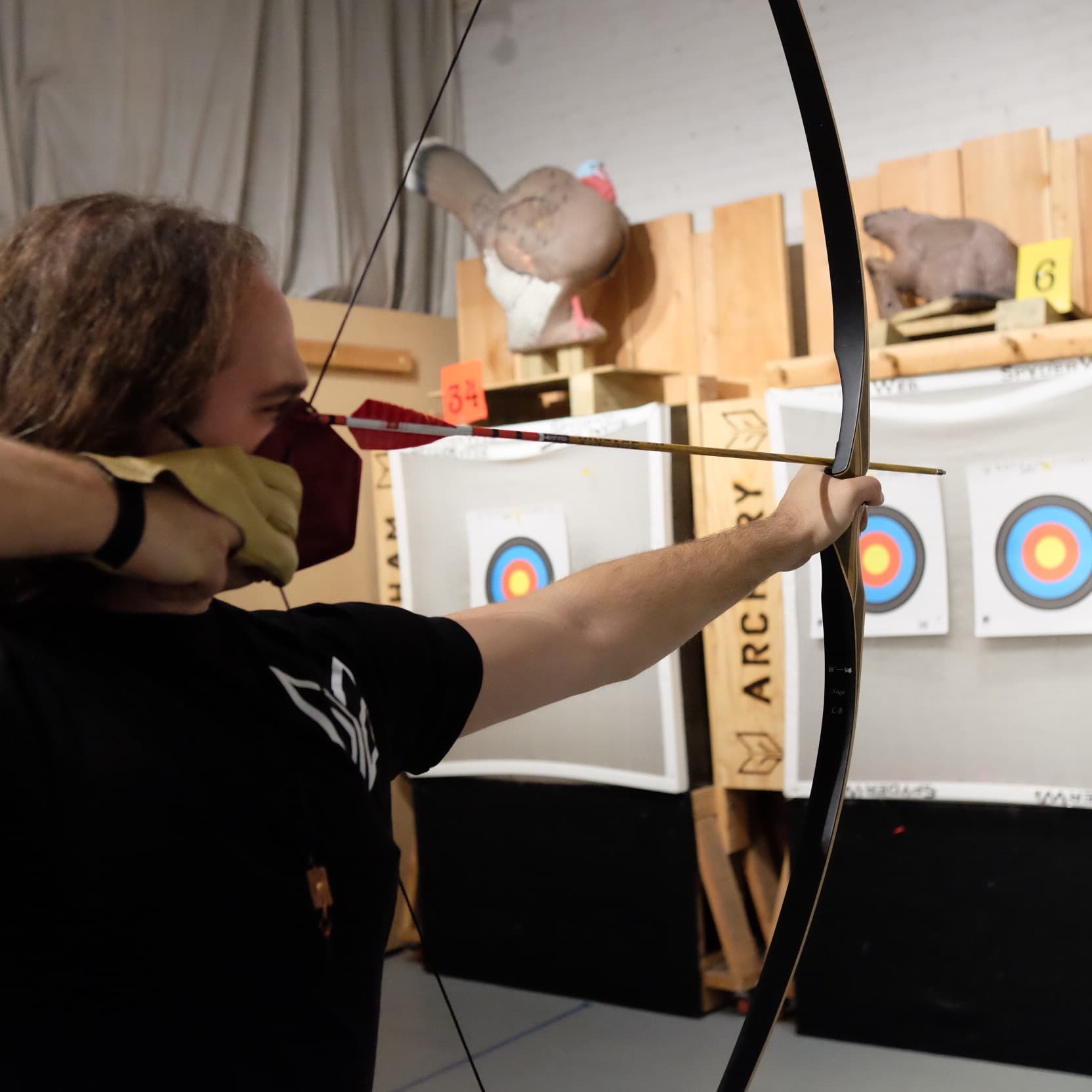 Archer drawing recurve bow indoors with targets in Brooklyn