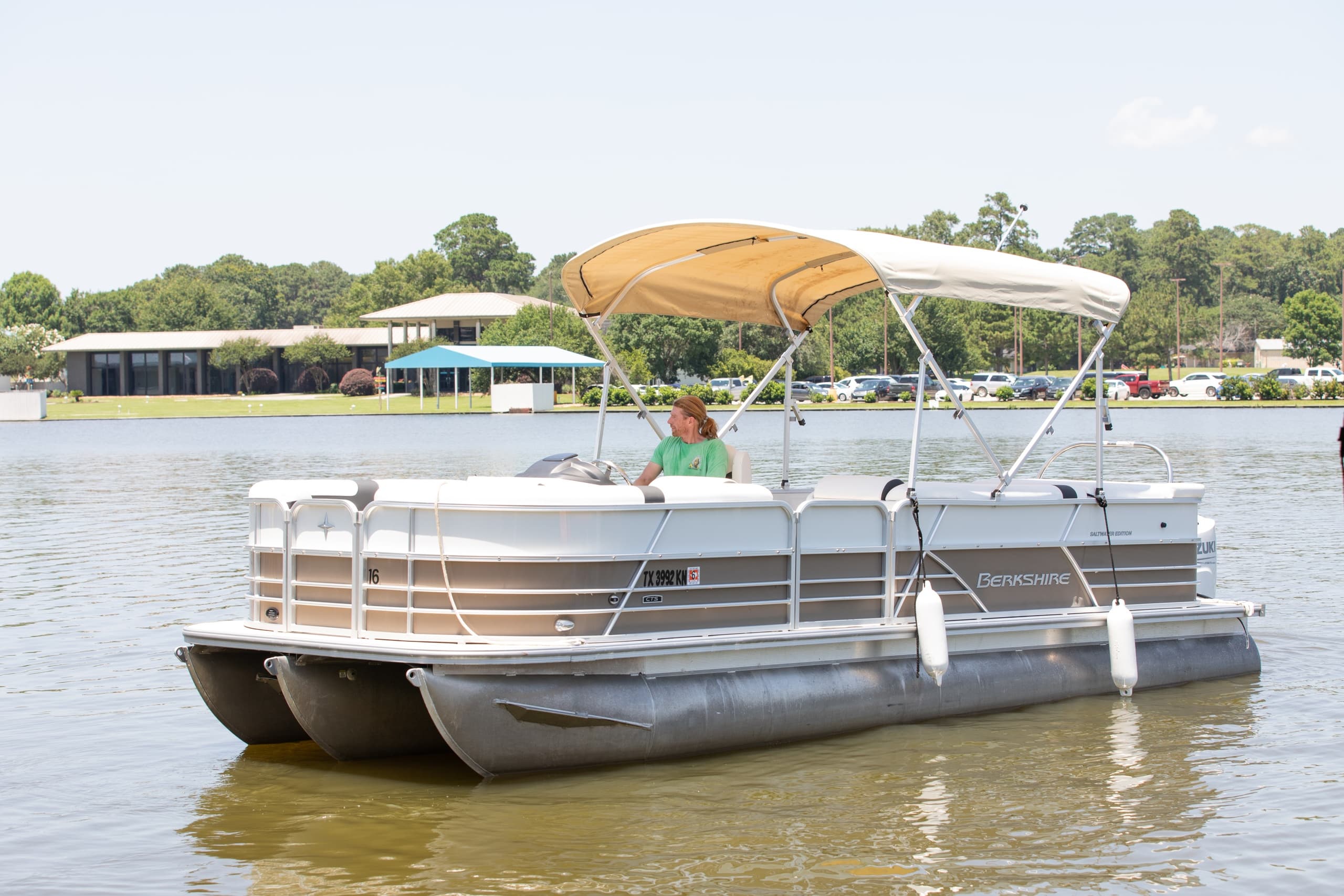 Covered pontoon boat anchored near shoreline at sunny lake