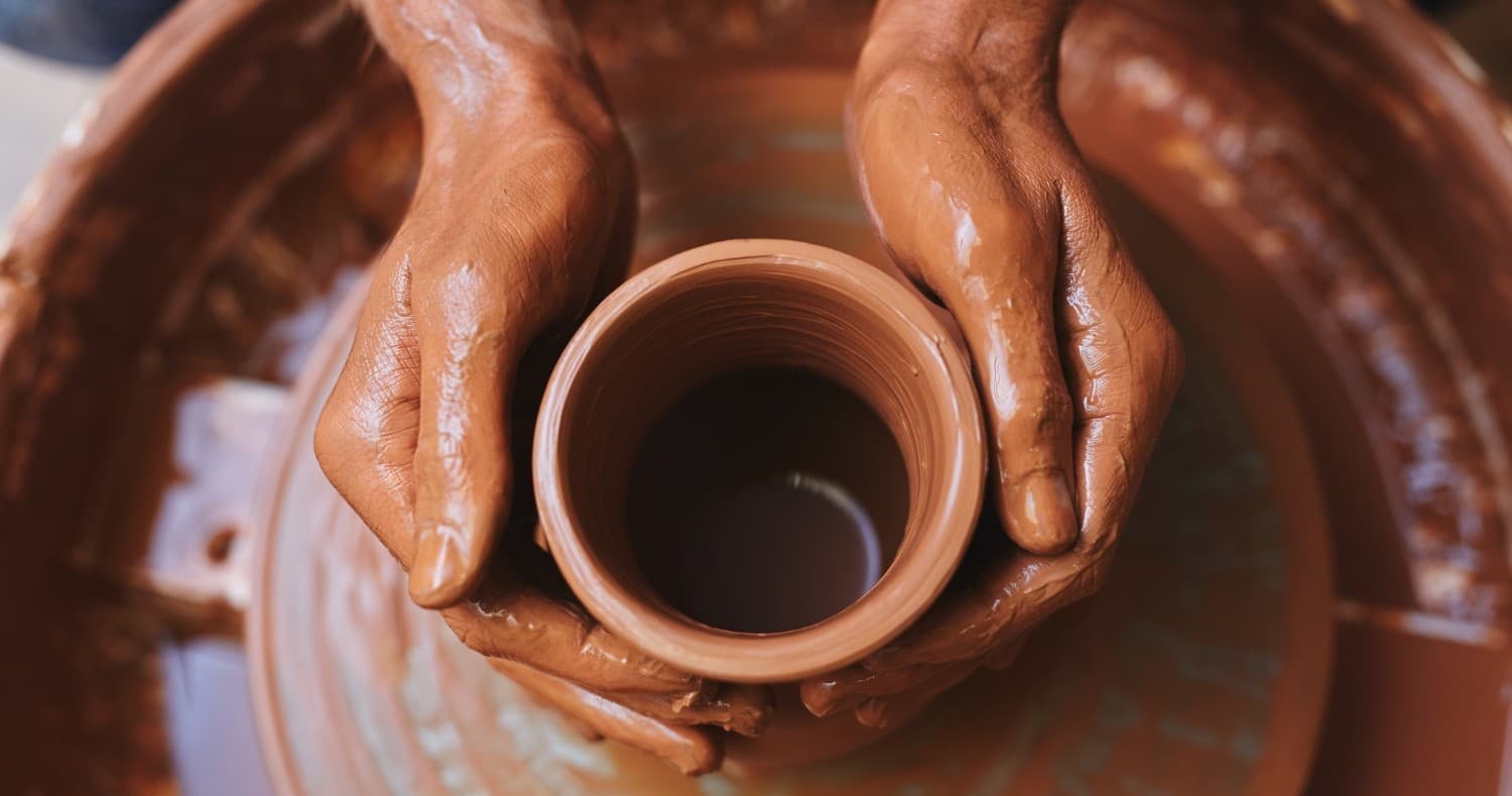 Hands shaping clay pot on pottery wheel in studio workshop
