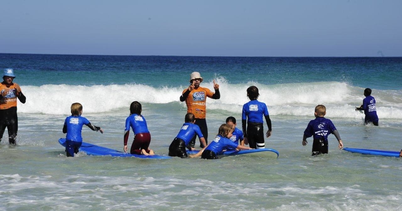 Surf school lesson with kids and instructor in shallow surf