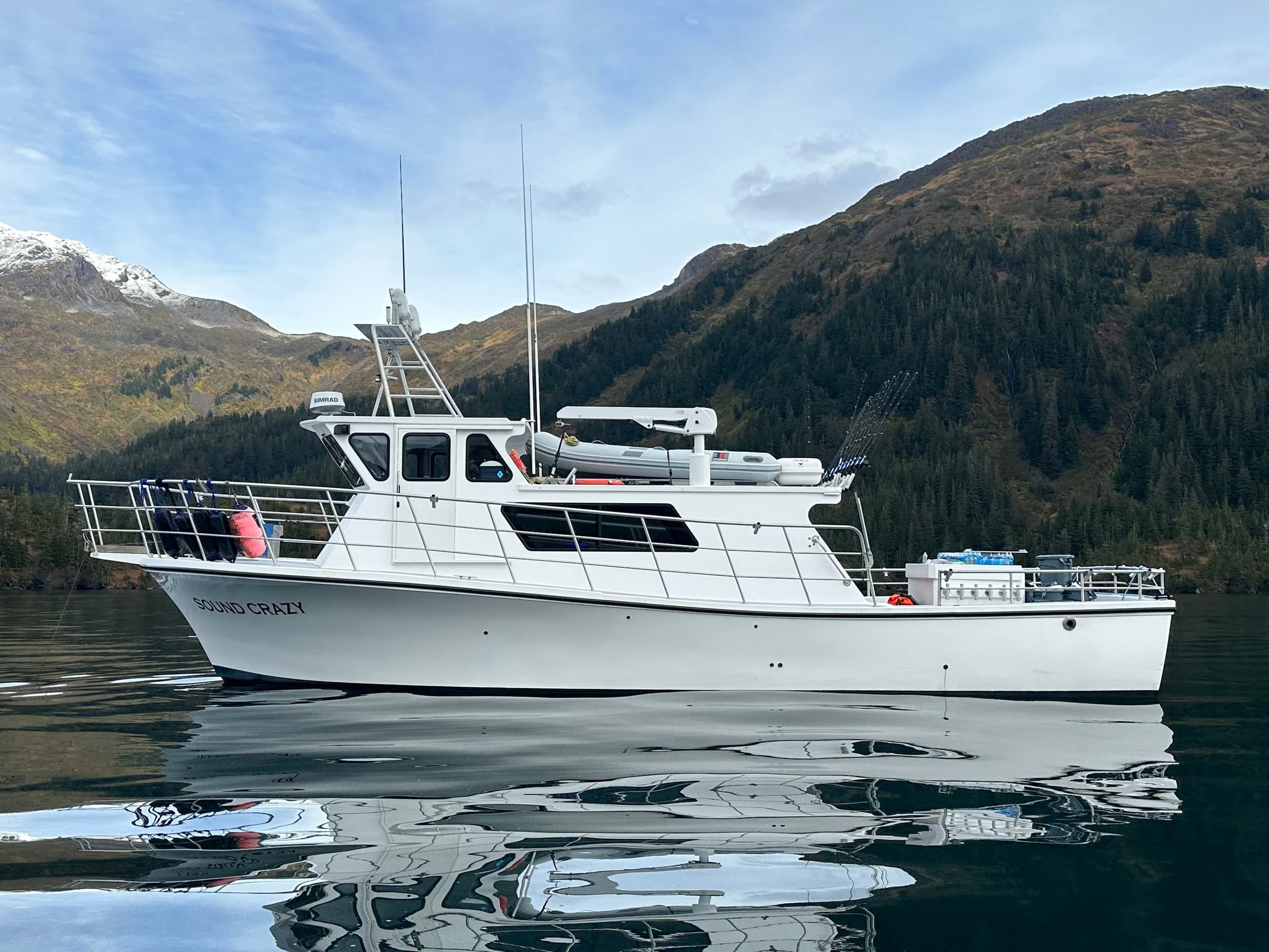 White charter yacht reflected in calm fjord waters with forested hills
