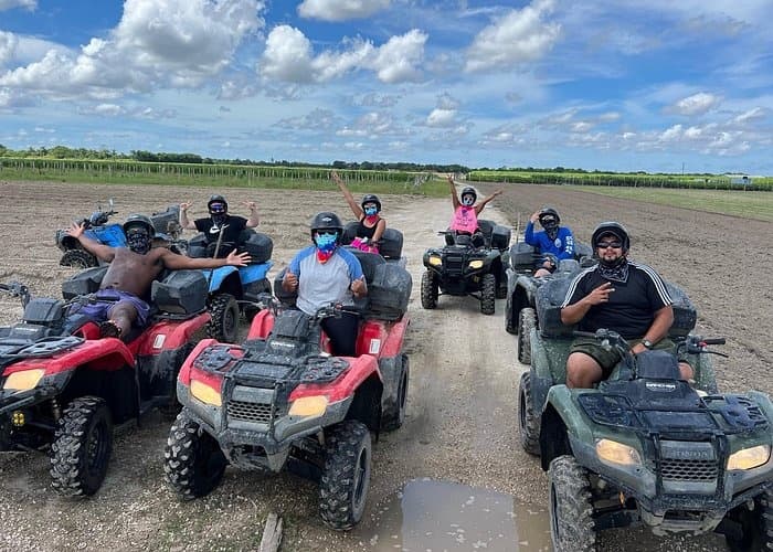 Group riding ATVs across muddy trails on open rural terrain