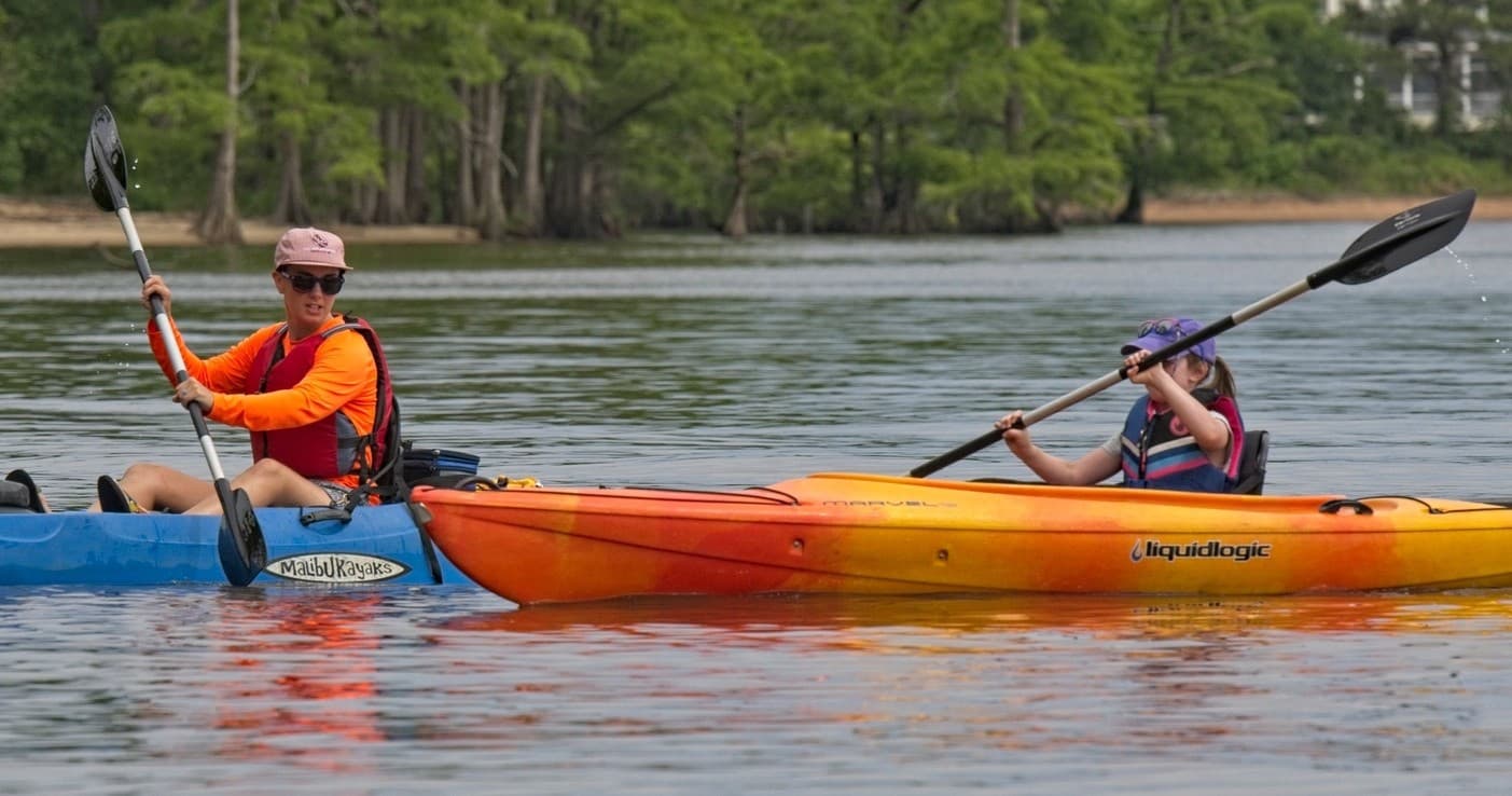 Recreational kayakers close-up paddling on calm bayou with cypress