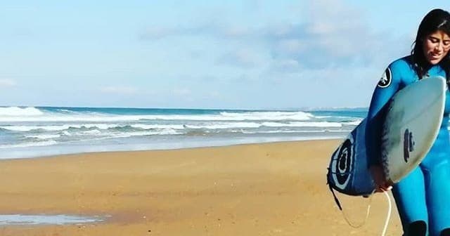 Surfer walking along sandy beach carrying blue surfboard