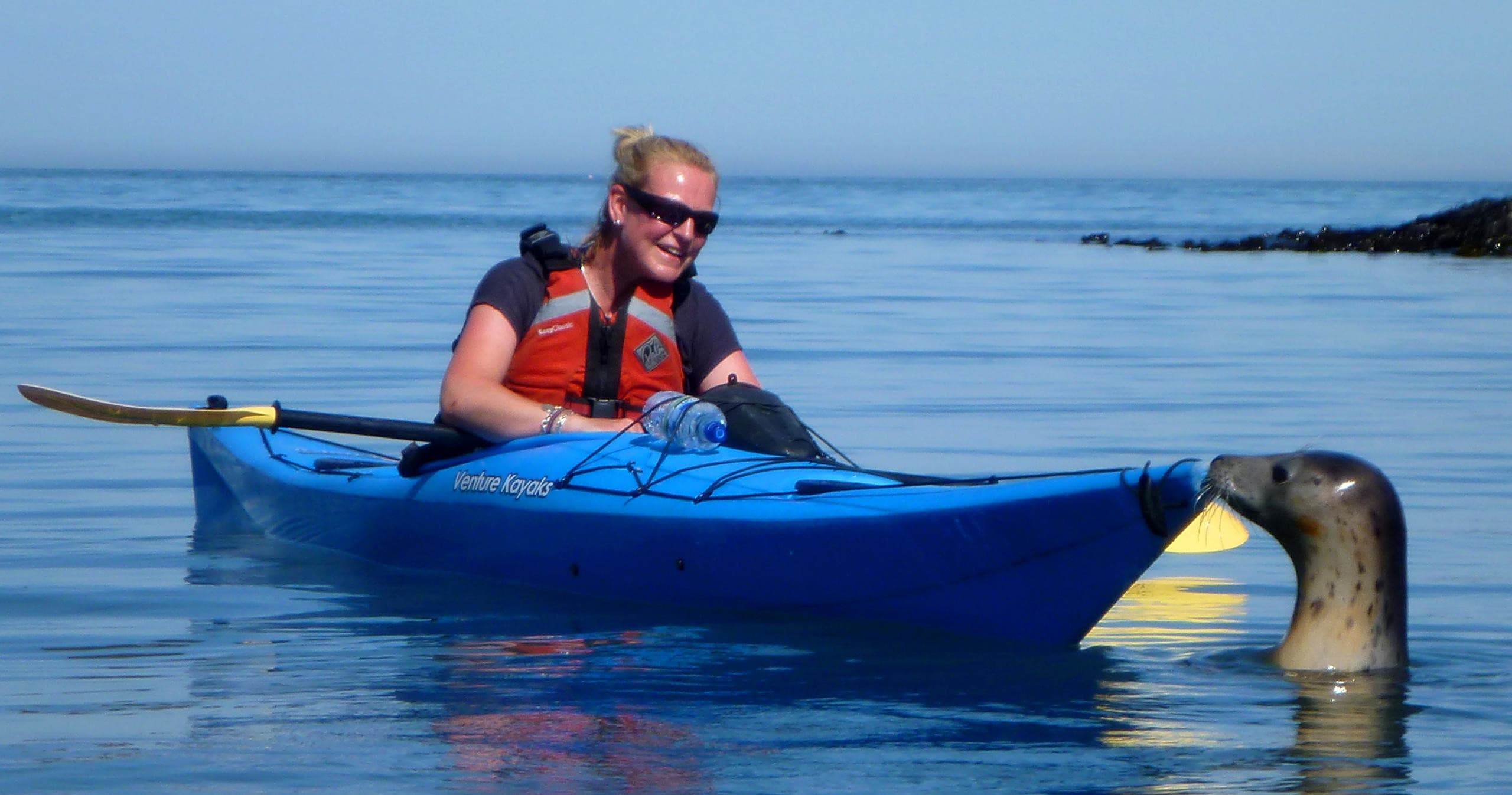 Solo kayaker paddling on calm sea under clear blue sky